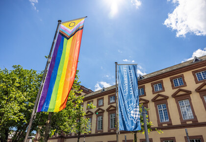 Vor dem Ostflügel des Mannheimer Schlosses wurde die Progress Pride Flag gehisst. Sie wird auch erweiterte Regenbogenflagge genannt. Daneben weht die dunkelblaue Fahne der Universität Mannheim.