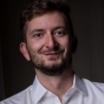 Portrait von Philipp Müller. Er trägt ein weißes Hemd und lächelt.