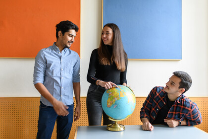 zwei Studenten und eine Studentin unterhalten sich in einem, auf dem Tisch steht ein Globus. Seminarraum