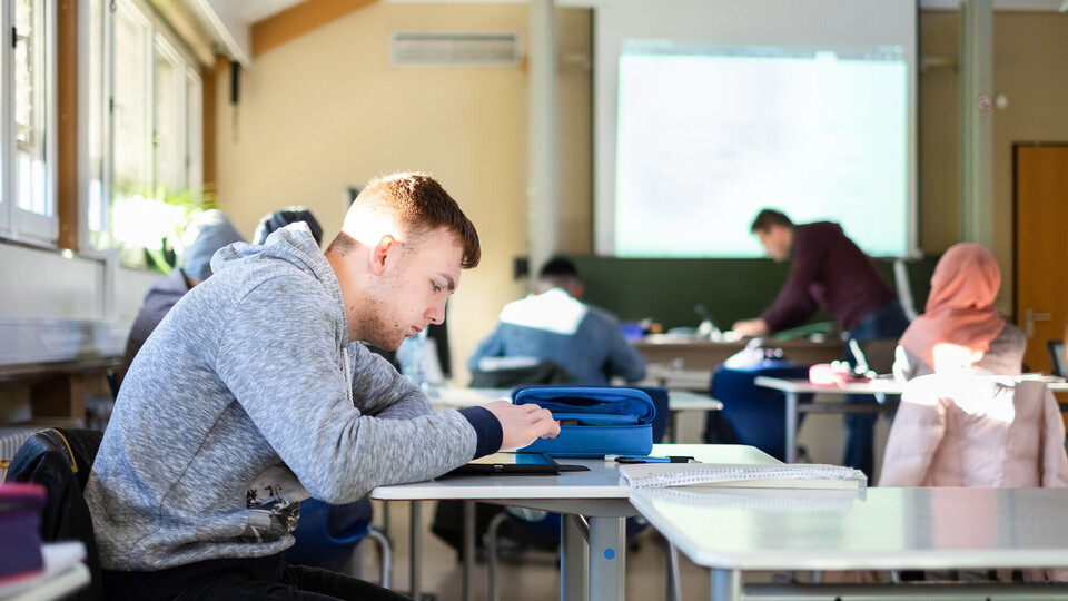 Schüler*innen arbeiten mit dem IPad im Klassenzimmer, vorne steht der Lehrer.