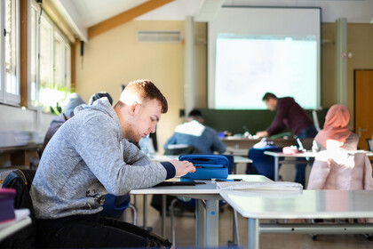 Schüler*innen arbeiten mit dem IPad im Klassenzimmer, vorne steht der Lehrer.