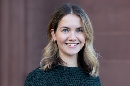 Klara Müller steht vor dem Mannheimer Schloss. Sie hat schulterlanges blondes Haar und trägt einen schwarzen Pullover.