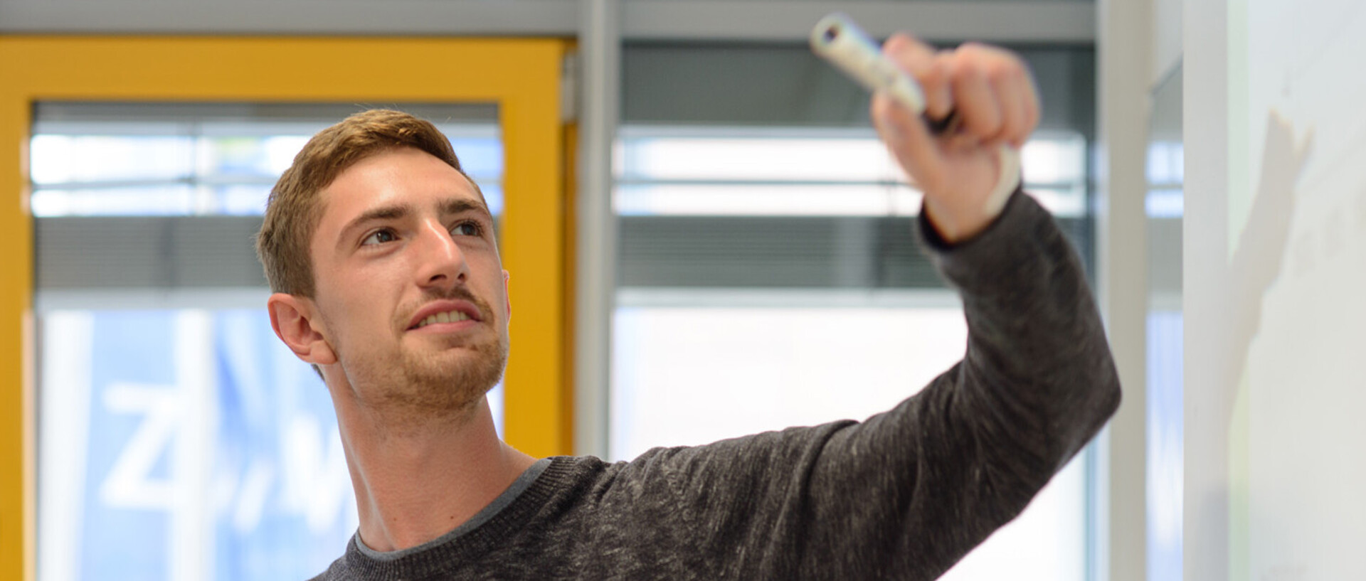 Ein Mann steht seitlich vor einem Whiteboard und zeigt mit einem Stift darauf.