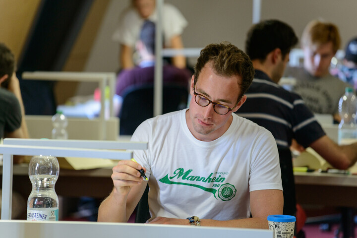 Ein Student sitzt mit Textmarker und Wasserflasche in der Bibliothek