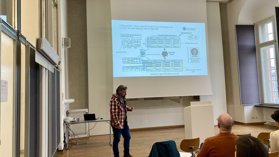 Dr. Marcus Kessel hält seinen Vortrag. Er trägt eine karierte Jacke und steht vor der Leinwand mit seiner Präsentation.