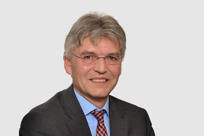 Prof. Spengel hat kurze graue Haare und eine Brille. Er trägt ein dunkles Jacket mit blauem Hemd und einer rot gemusterten Krawatte.