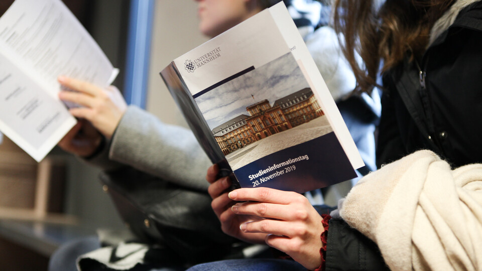 Zwei Studierende sitzen beisammen und lesen eine Broschüre zum Studieninformationstag. 
