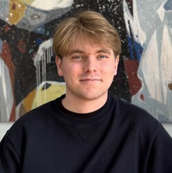 Portät des Studenten Alrik Schulze. Alrik Schulze hat blaue Augen und blonde Haare, die ihm in die Stirn fallen. Er trägt einen schwarzen Pullover und lächelt freundlich.