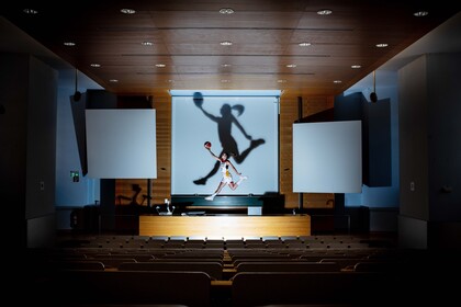 Eine Basketballerin springt in einem Hörsaal mit Ball in die Luft. 