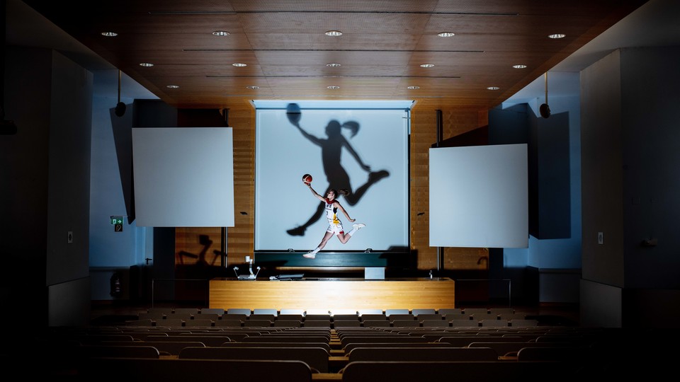 Eine Basketballerin springt in einem Hörsaal mit Ball in die Luft. 