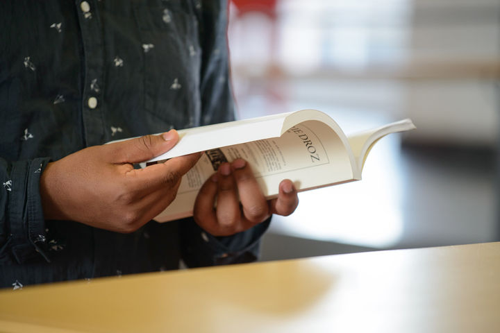 Ein Student hält ein aufgeschlagenes Buch in seinen Händen.