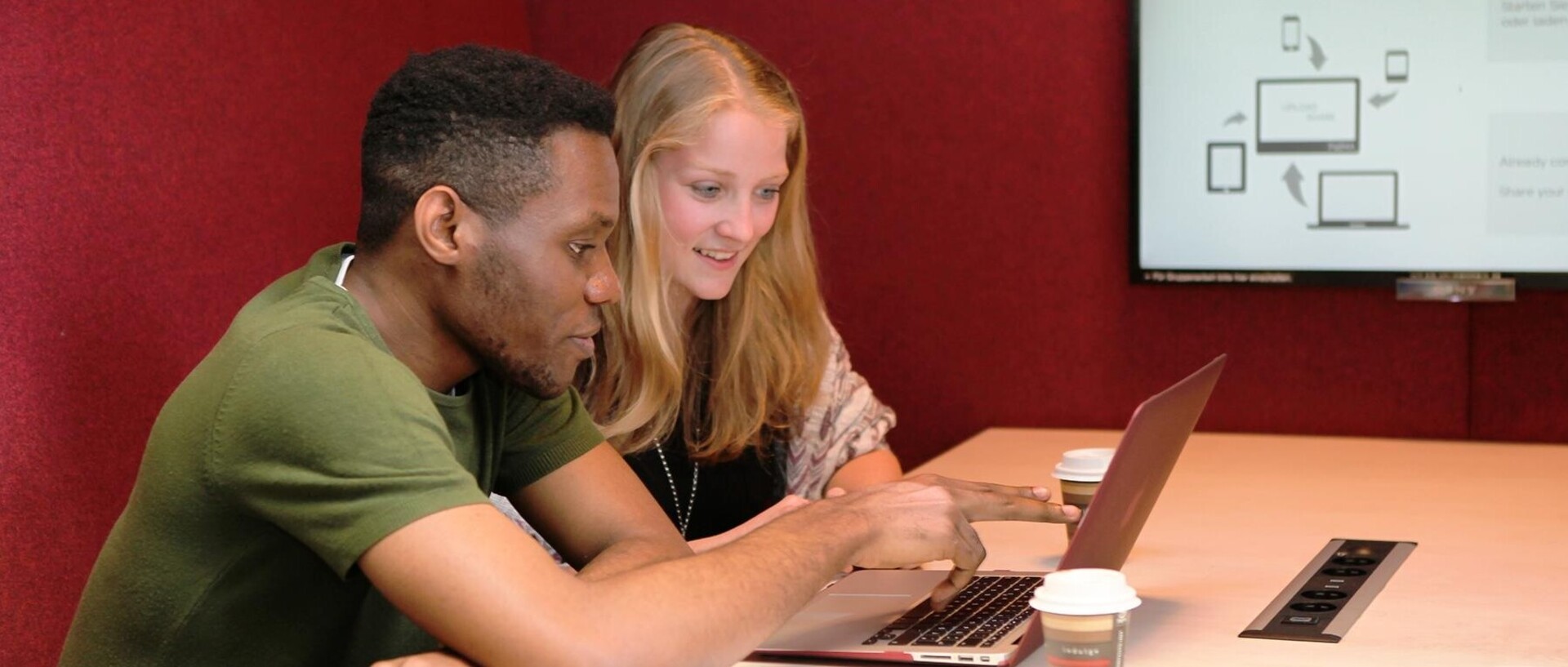 Ein Student und eine Studentin sitzen gemeinsam im Learning Center und blicken auf einen Laptop.