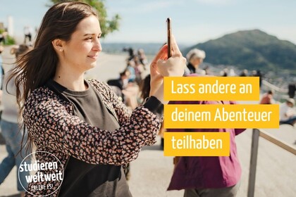 Frau macht im Freien ein Foto mit dem Smartphone; im Bild hervorgehoben der Text ‚Lass andere an deinem Abenteuer teilhaben‘ und ein ‚studieren weltweit – Erlebe es!‘-Logo.