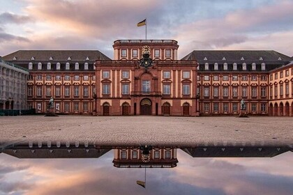 Blick auf die Universität Mannheim bei Sonnenuntergang. Davor spiegelt sich das Schloss in einer Pfütze Wasser.