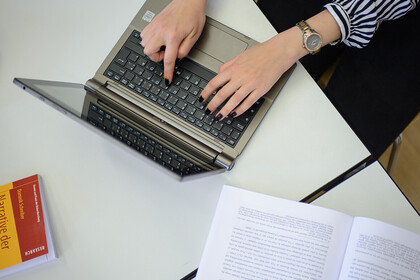 Zwei Hände einer Frau tippen auf der Tastatur eines Laptops.