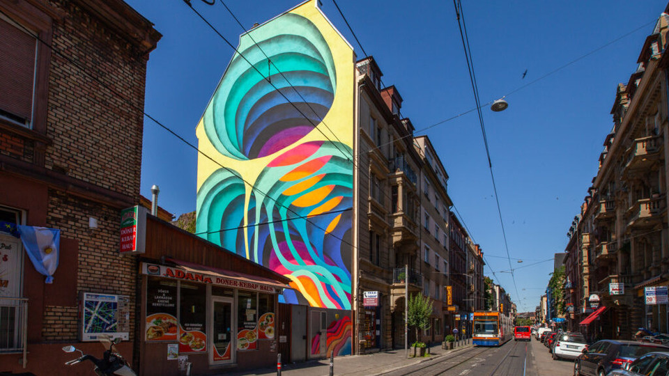 Eine Hauswand ist bunt bemalt. Daneben velaufen Straßenbahnschienen. 