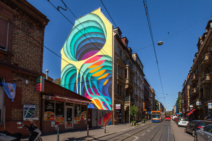 Eine Hauswand ist bunt bemalt. Daneben velaufen Straßenbahnschienen. 