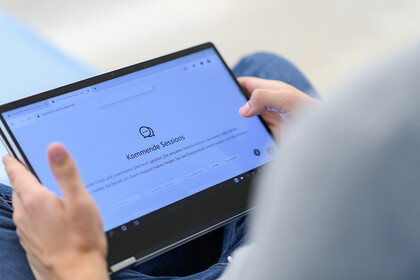 Ein Mann hält seinen Laptop auf dem Schoß fest und tippt auf das Display.