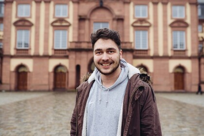 Marco Rupp hat kurze braune Haare und einen dunklen Bart. Er trägt einen grauen Kapuzenpullover und darüber eine rote Jacke.