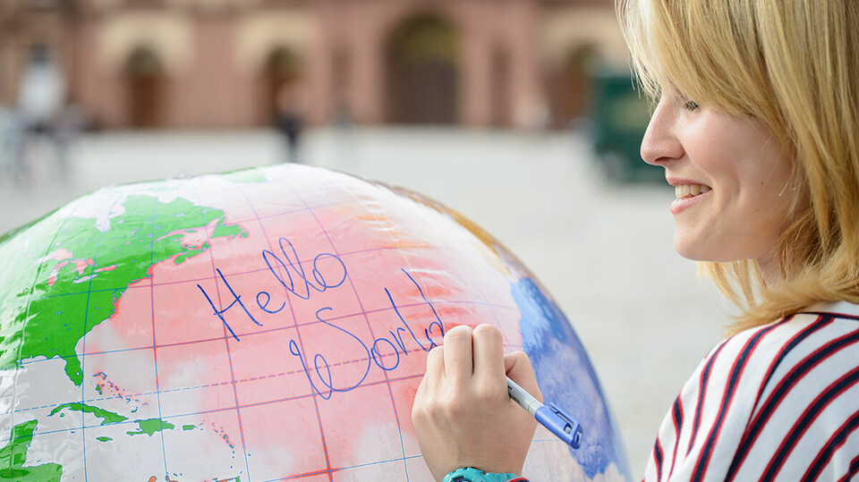Eine junge Frau schreibt auf eine Weltkugel die Wörter "Hello World".