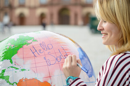 Eine junge Frau schreibt auf eine Weltkugel die Wörter "Hello World".