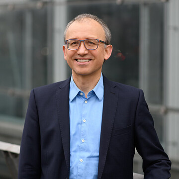 Portrait of Professor Thomas Gschwend, Ph.D. He is wearing a blue shirt with a dark jacket over it and is leaning against a railing.