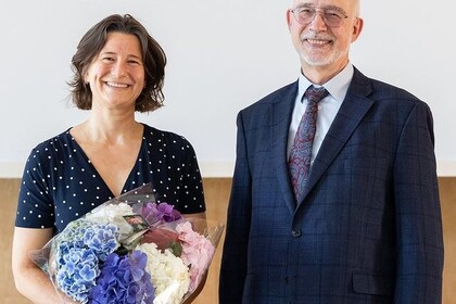 Die neu gewählte Kanzlerin Dr. Katrin Schoppa-Bauer links neben dem Rektor Prof. Dr. Thomas Puhl. Beide lachen glücklich in die Kamera. Sie hält einen bunten Blumenstrauß in den Händen. Sie trägt ein blaues Kleid mit weißen Punkten und die halblangen, dunklen Haare offen. Er trägt eine Brille und einen Bart und die Haare sehr kurz. Außerdem trägt er einen dunkelblauen Anzug mit blauer Krawatte und weißem Hemd. Link: Instagram-Post zu neue Kanzlerin der Universität Mannheim gewählt