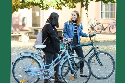 Zwei Studierende stehen mit ihren Fahrrädern auf dem Schneckenhof und unterhalten sich. Oben links steht "Green Uni Ma".