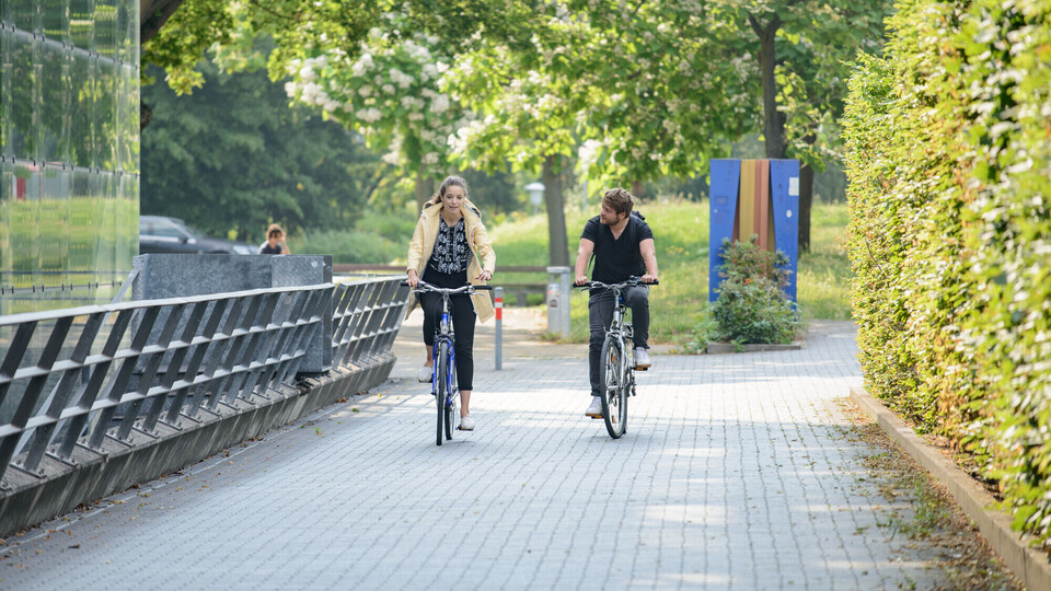 Eine Studentin und ein Student fahren Rad. Sie sind vor dem Gebäude A5.