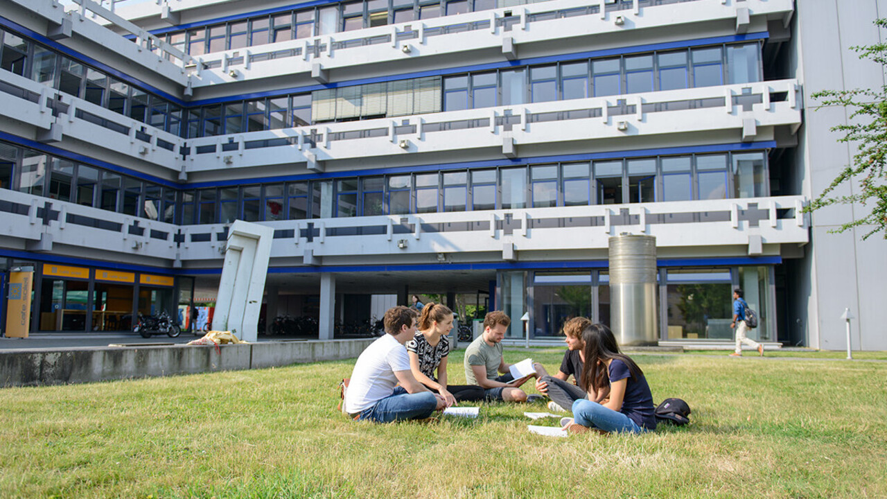 Studierende sitzen auf einer Wiese vor dem A5-Gebäude uns lernen gemeinsam mit Büchern.