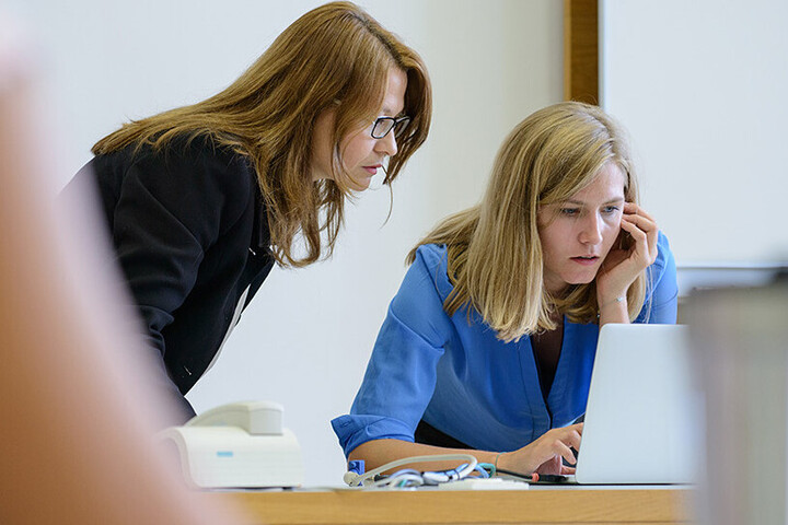 Zwei Frauen sind über einen Bildschirm eines Laptops gebeugt.