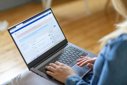 Eine junge Frau hat ihren Laptop auf dem Schoß und arbeitet.