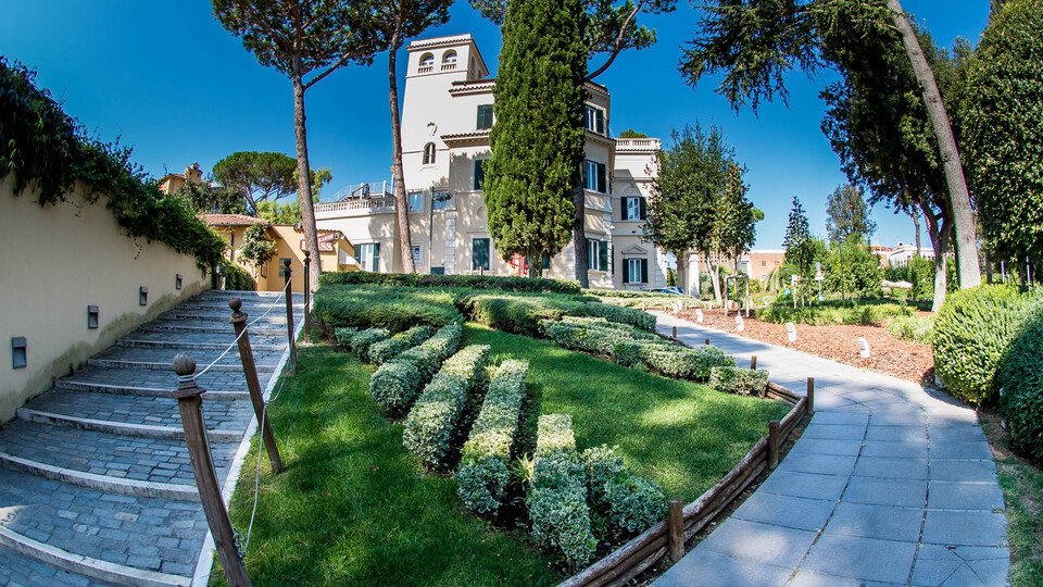 Gartenanlage mit Grünfläche und Wegen und Gebäude im Hintergrund