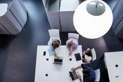 Drei Studierende sitzen an einem Arbeitstisch mit Schreibmaterial und Computer nebeneinander, fotografiert von oben in dem B6-Gebäude. 