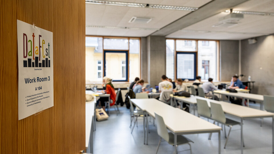 Blick in einen Seminarraum, in dem Studierende konzentriert an Laptops arbeiten. An der Tür hängt das DataFest-Logo