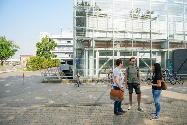 Drei Studierende stehen gemeinsam vor dem A5-Gebäude und unterhalten sich. 