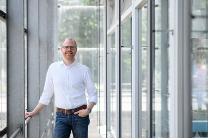 Eine Person trägt ein weißes Hemd sowie eine blaue Jeans und steht in einem Flur. Die Person heißt Jochen Gebauer.