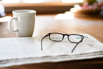 Auf einem Tisch liegt eine Zeitung und eine Brille neben einer Kaffeetasse