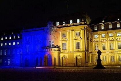 Aufnahme der Universität Mannheim bei Nacht. Die linke Hälfte des Mittebaus und der Ostflügel leuchten blau. Die rechts Seite des Mittelbaus und der Westflügel leuchten gelb.