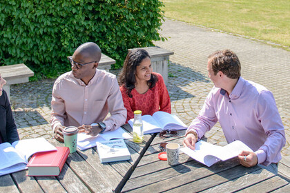 Bild von Studierenden im Freien an Holztisch