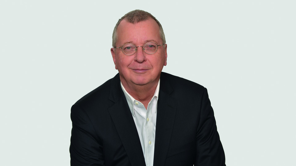 Prof. Weber hat kurze Haare und eine Brille. Er trägt ein dunkles Jacket und ein weißes Hemd. 