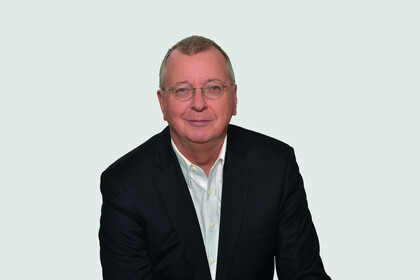 Prof. Weber hat kurze Haare und eine Brille. Er trägt ein dunkles Jacket und ein weißes Hemd. 