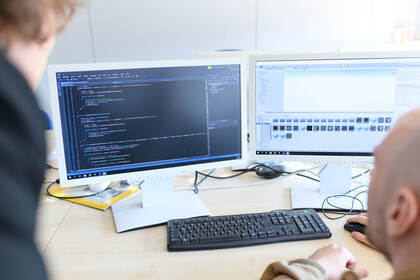 Zwei Personen betrachten zwei Bildschirme. 