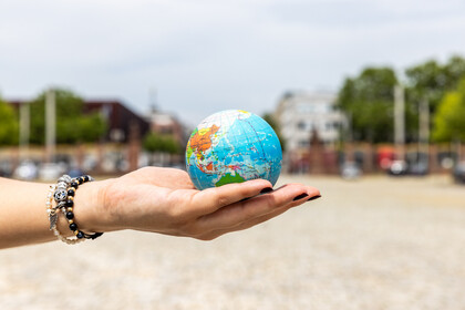 Student holding a globe in the palm of her hand. She is wearing three bracelets in black and silver and has black nail polish. 