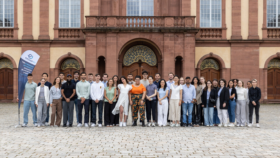 Gruppenbild von Studierenden, die im Ehrenhof des Schlosses Mannheim nebeneinander stehen und in die Kamera blicken.