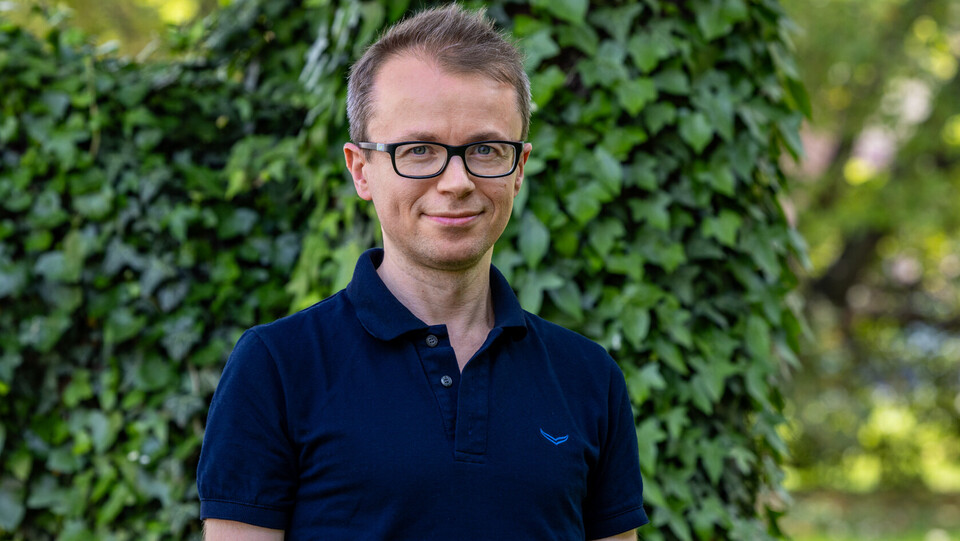 Dr. Peter Parczewski in dunkelblauem Poloshirt vor einem Hintergrund mit grünen Pflanzen und Bäumen.
