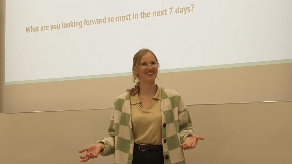 Frau lächelt in die Kamera und steht vor einer Powerpoint-Präsentation