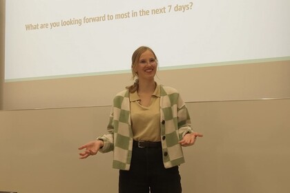 Frau lächelt in die Kamera und steht vor einer Powerpoint-Präsentation