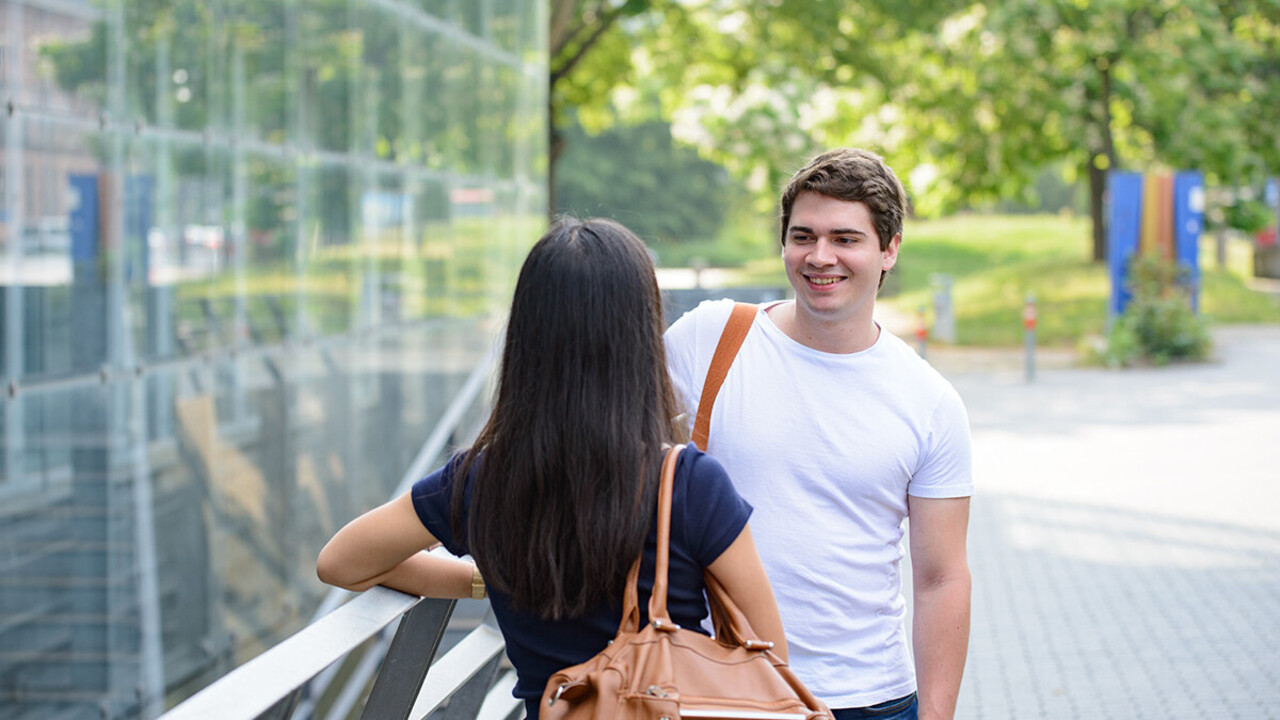 Zwei Studierende stehen gemeinsam vor dem A5-Gebäude und unterhalten sich.
