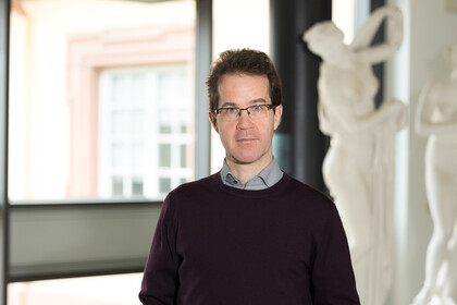 Prof. Dr. Christian Mann hat kurze braune Haare und eine Brille. Er trägt einen braunen Wollpullover.
